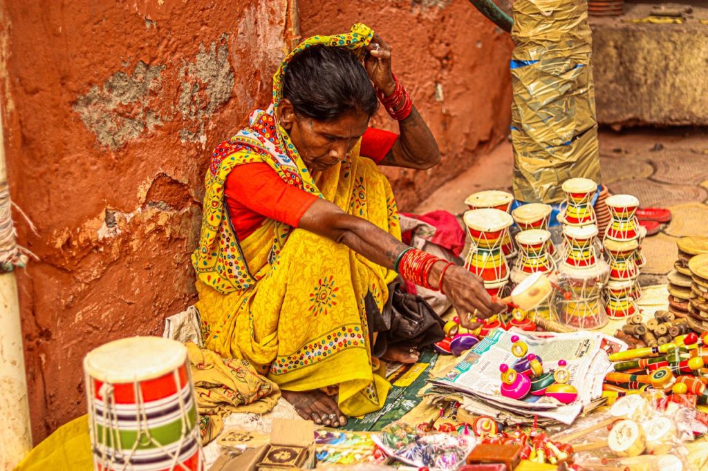 Woman in vibrant attire selling traditional toys on a street market, showcasing cultural heritage.